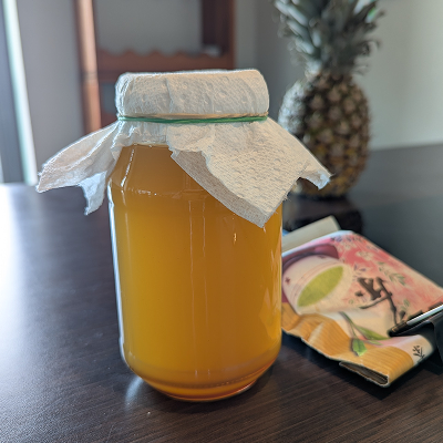 A jar of Jun brewing on the counter, with a pineapple and green tea leaves in the background